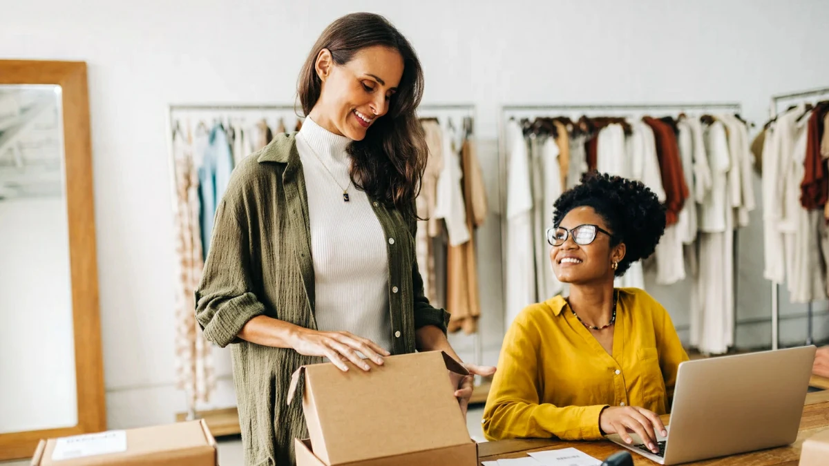 Two female entrepreneurs happily managing orders for their online clothing store, illustrating dropshipping, e-commerce, and business growth.